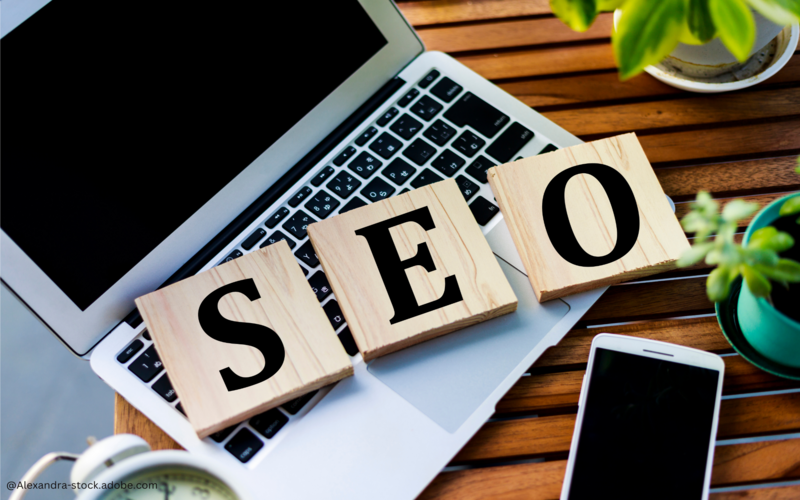 Drei beschriftete Holzquadrate liegen auf einem Laptop, sie bilden das Wort SEO
