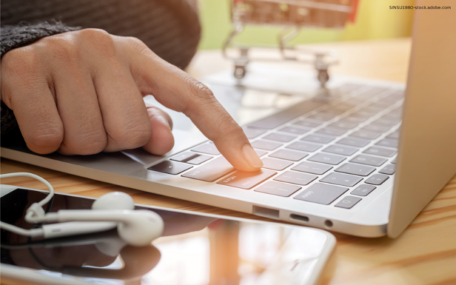 Man sieht einen Finger auf der Tastatur eines Laptops liegen, daneben liegen Kopfhörer und ein Handy.